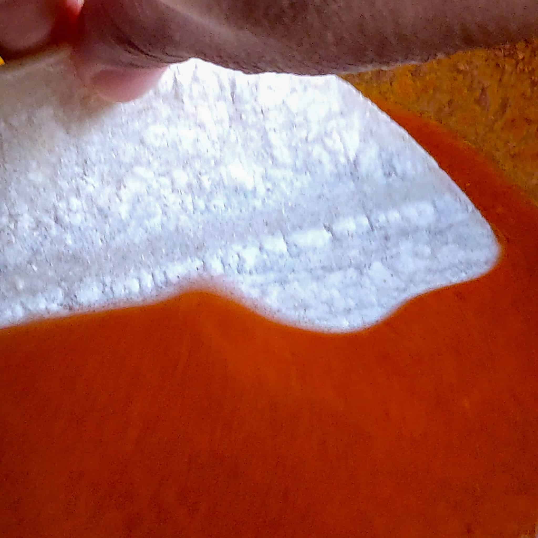 corn tortilla being dipped in the birria consume sauce.